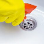 Main avec gant nettoyant une douche italienne pour déboucher l’évacuation de l’eau.