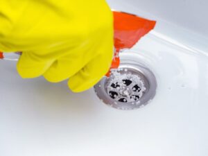 Main avec gant nettoyant une douche italienne pour déboucher l’évacuation de l’eau.