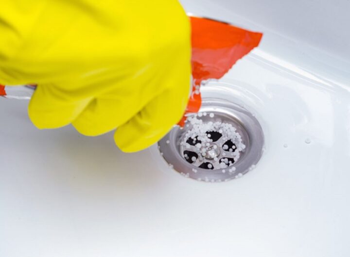 Main avec gant nettoyant une douche italienne pour déboucher l’évacuation de l’eau.